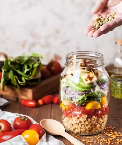 탁자위에 각종 야채&#44;채소 과일이 올려져있고 유리병에 이곡물및채소 과일등을 손으로 담는 모습