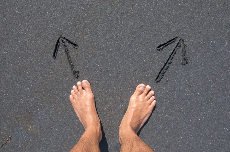A pair of bare feet on Bali's beach sand with arrows drawn, symbolizing choice and direction.