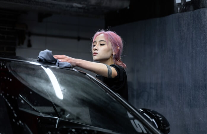 핑크색으로 염색한 머리의 젊은 여자가 세차를 하고 있는 모습