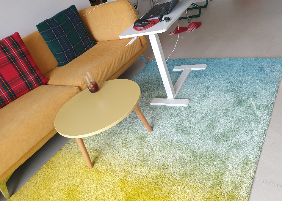 바닥에 노란색에서 청색으로 그러데이션 되는 카펫과 흰색 사이드 테이블이 있다.