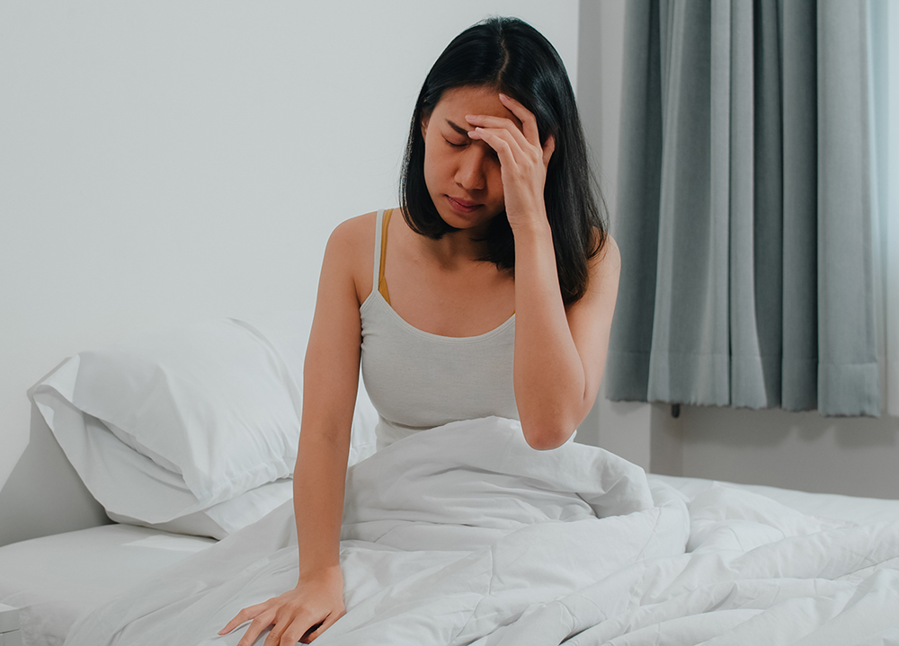 한 여성이 침대 위에서 잠이 들지 않아 손을 이마에 댄 채로 괴로워 하고 있는 사진