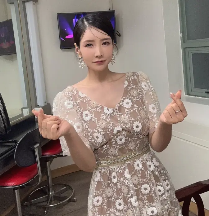 현역가왕- 가슴이 깊게파인 꽃무늬 원피스를 입고 손으로 작은 손하트를 하고 포즈를 잡고있는 한봄