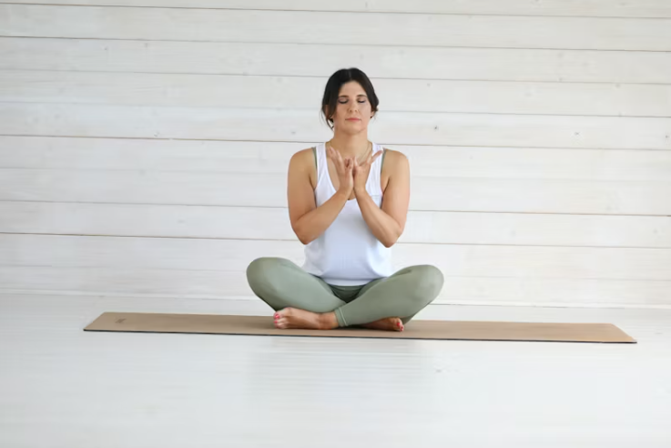 요가 매트 위에서 명상 중인 여성 &ndash; 두 손을 가슴 앞에 모으고, 눈을 감고 편안하게 호흡하는 모습.