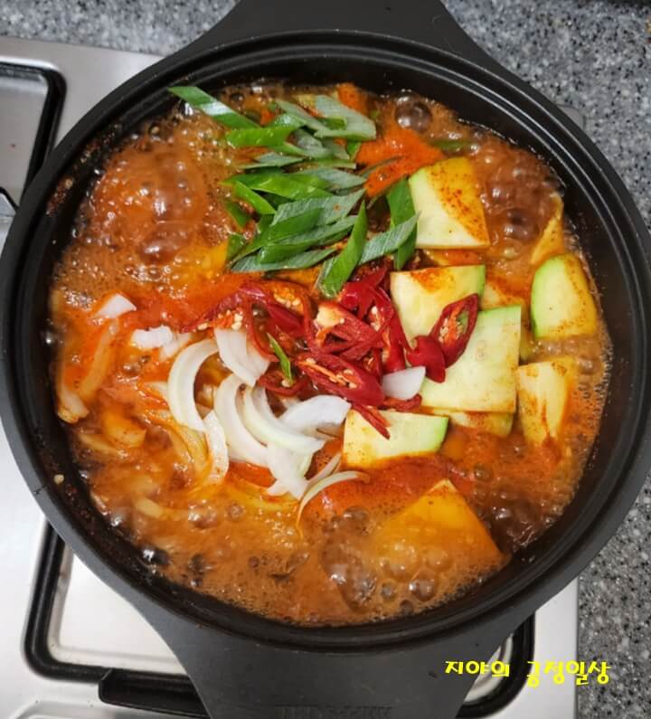 끓고 있는 빨간 양념장 위에 올린 호박, 대파, 양파, 빨간 고추