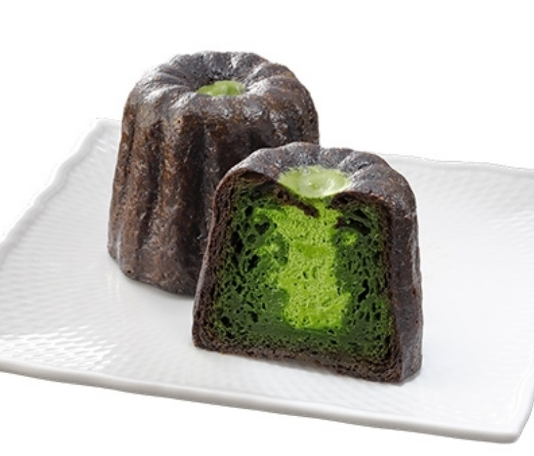 겉에는 검은색 초콜릿으로 감싸져 있고 안에는 초록색 녹차가 들어가 있는 원형의 디저트가 반으로 갈라져 흰색 그릇위에 올려져 있다.