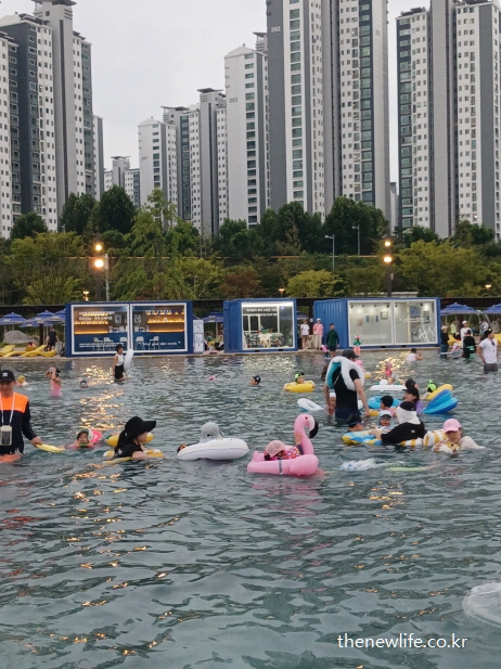 잠실 한강공원 물놀이장에서 튜브를 탄 아이들과 함께 수영장 중앙에서 물놀이를 즐기는 가족들의 모습