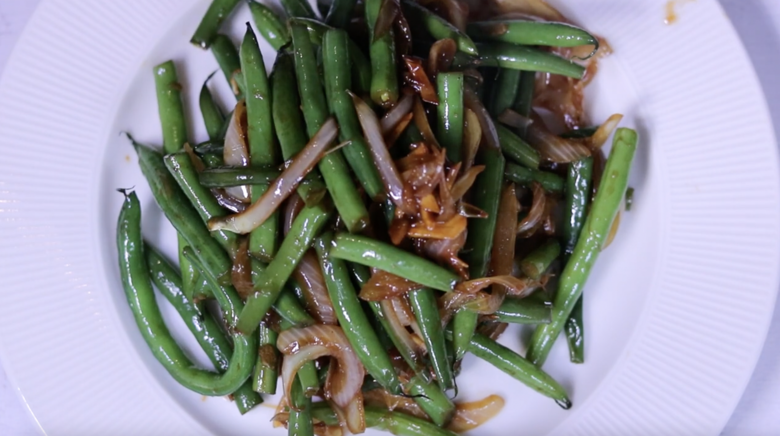 둥근 흰색 접시에 볶은 양파 그린빈을 담은 사진