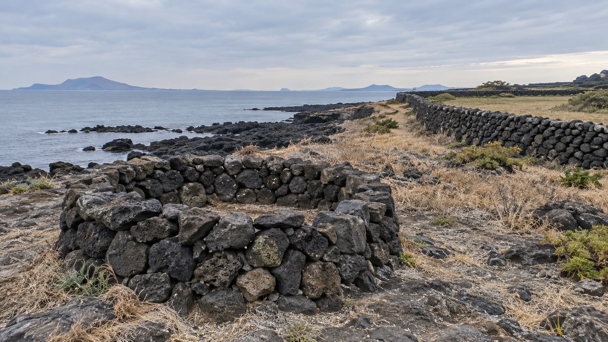 Illustration of a round basalt haenyeo bulteok enclosure and a field stone wall on Jeju's coast, AI-generated and not the actual site