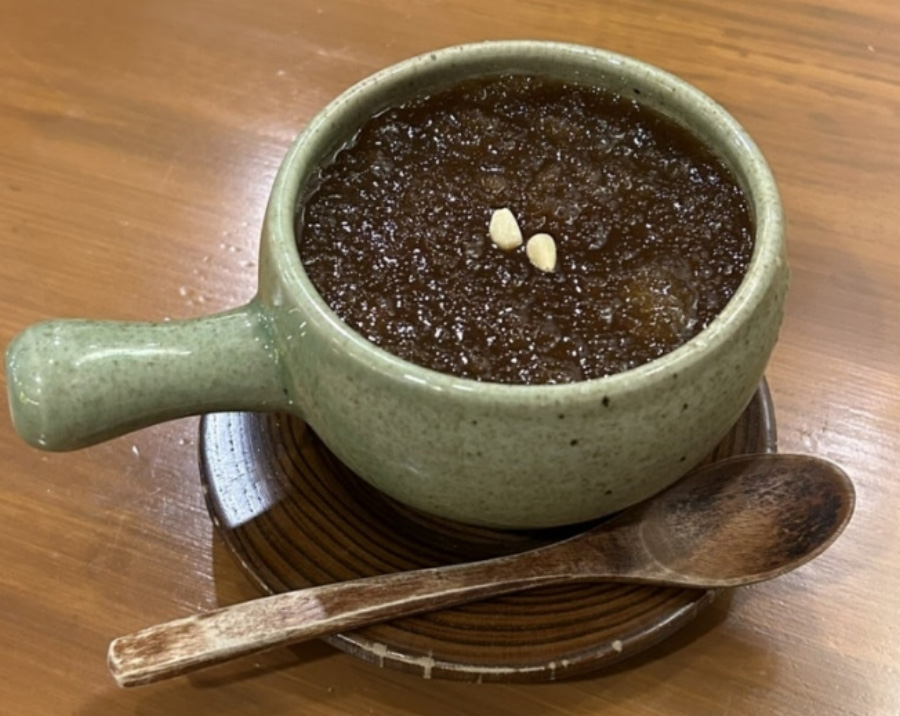 나무 테이블 위에 고동색의 동그란 찻잔받침대 위에 제호탕을 가득 담은 쑥색의 찻잔과 고동색의 나무숟가락을 두고 찍은 사진