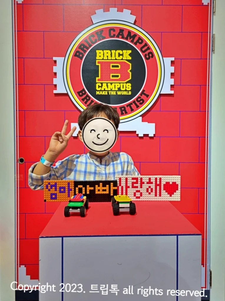 빨간 별돌을 배경으로 챔피온이라는 영어가 적혀있고 그 앞에선 아이가 엄마아빠사랑해라는 푯말과 자동차 2대를 놓고 사진을 찍는다