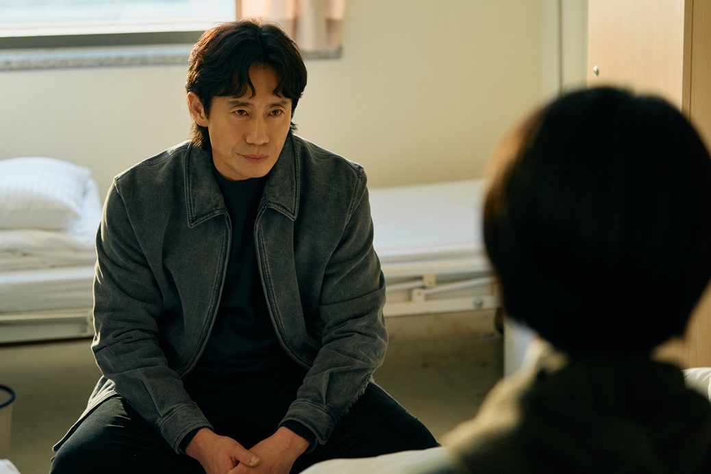 병실에서 상대 인물과 마주 앉아 이야기하는 정호명 역 신하균의 오십프로 공식 스틸