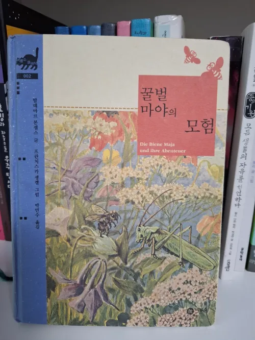 햇살 가득한 들판에서 홀로 야생화 위에 앉아 있는 꿀벌 마야. 집단주의를 벗어난 자아 발견과 지적 자립의 시각화. (Maya the bee exploring wildflowers alone in a sun-drenched meadow, visualizing self-discovery beyond collectivism and intellectual self-reliance.)