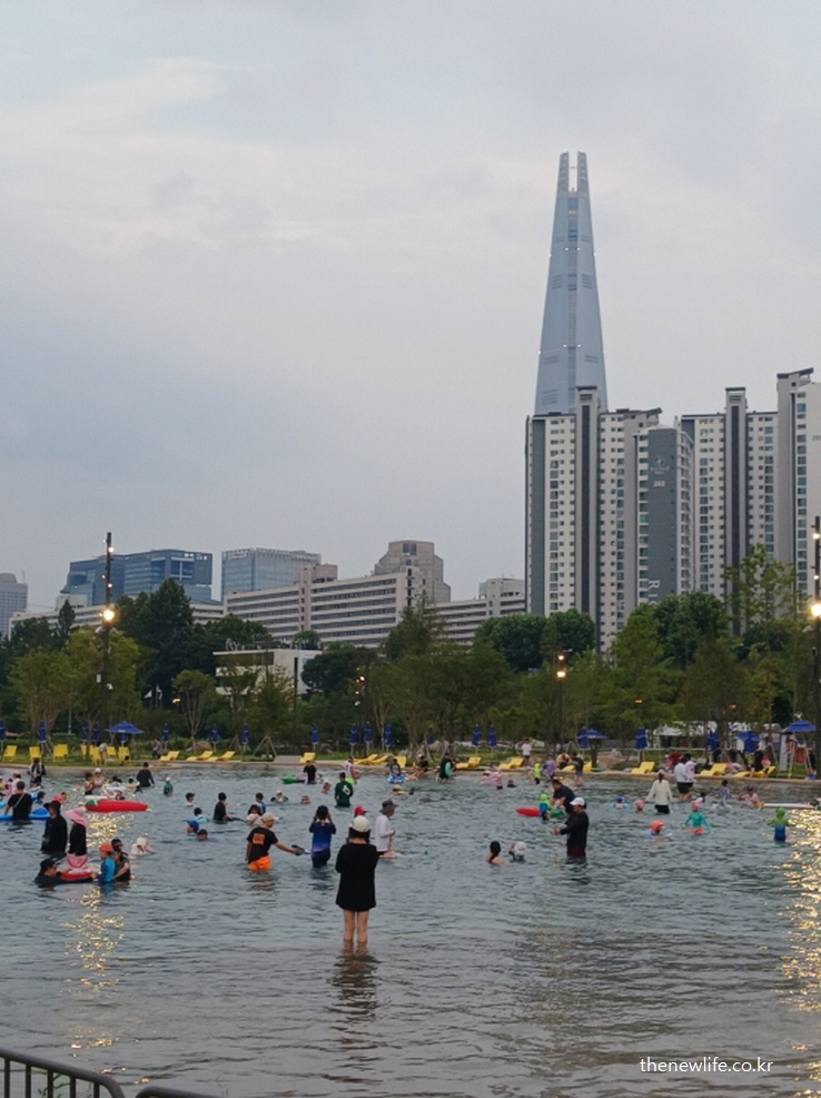 잠실 한강공원 물놀이장과 롯데타워를 배경으로 시민들이 물놀이를 즐기는 풍경 – 도심 한복판의 여름