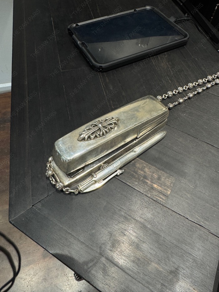 A luxury Chrome Hearts sterling silver stapler object placed on a dark wooden table⁠