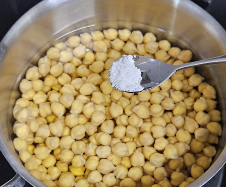 충분히 불린 병아리콩이 냄비에 물과 함께 담겨있고 여기에 소금을 넣고 있다