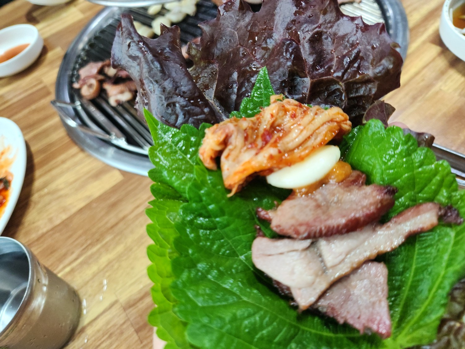 상추와 깻잎 위에 마늘&amp;#44; 김치&amp;#44; 쌈장&amp;#44; 고기를 올린 모습
