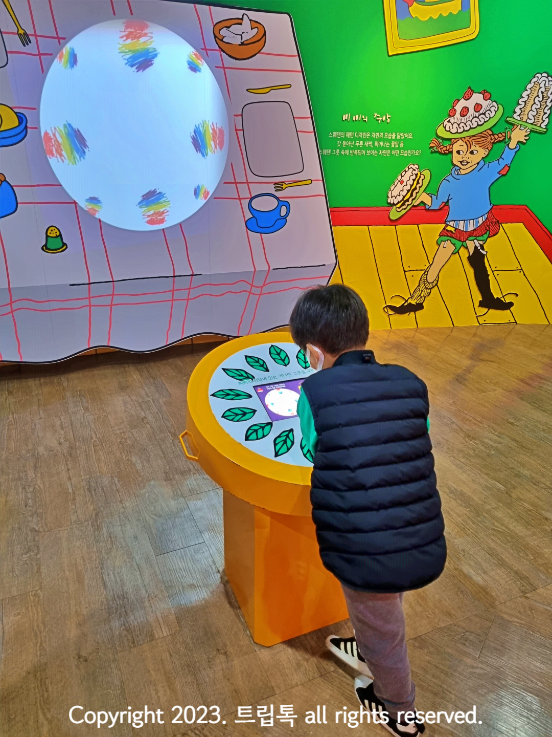 아이가 노란 테이블에 기대 그림을 그리고 그 그림이 화면에 표시되고 있다.