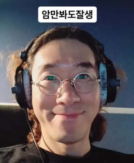 싱어게인3- 파란벽지 앞 검은의자에 앉아 헤드폰을 끼고 미소지으며 머리맡에 쓰인 흰바탕 검은글씨 암만봐도잘생