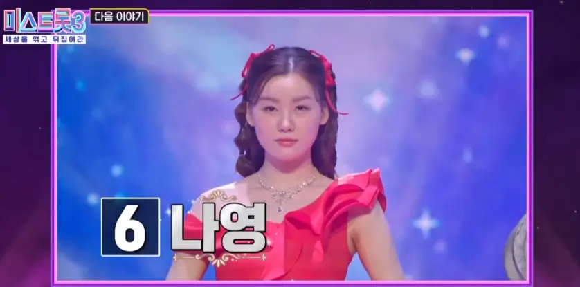 미스트롯3-
보라색 배경 가운데 밝은 보라색 무대 가운데 빨간 드레스에 긴곱슬머리를 늘어뜨린 채 왼쪽 하단 검은 네모 안 흰클씨 6 검은네모 밖 흰글씨 나영