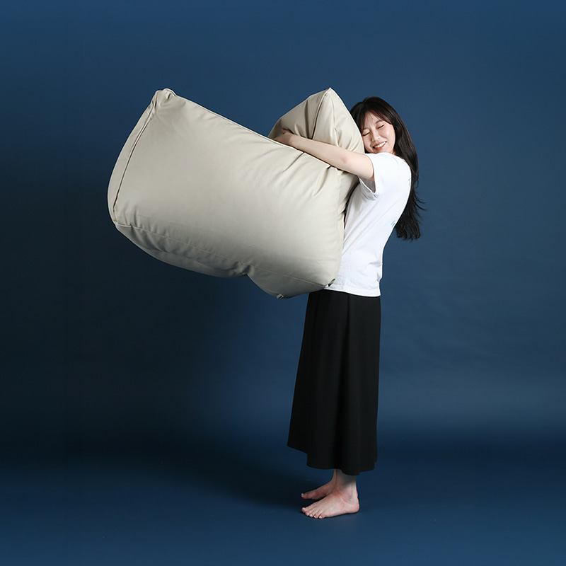 남색 배경 앞에서 흰 티셔츠를 입은 사람이 아이보리 계열 플래지어 톰빈백 기능성 가죽 빈백을 두 팔로 안아 들어 올린 모습