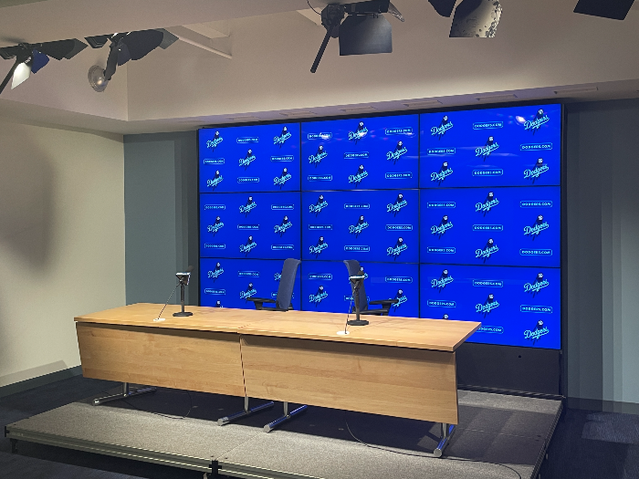 인터뷰 룸. 다저스 마크가 작은 글씨로 여러 개 새겨진 파란 스크린이 있고, 그 앞으로는 테이블과 의자 두 개와 마이크 두 개가 있다. 선수들은 파란 배경 앞 의자에 앉아 인터뷰를 진행한다.