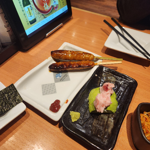 테이블 위에 꼬치 두 개와 명란 아보카도가 보인다.