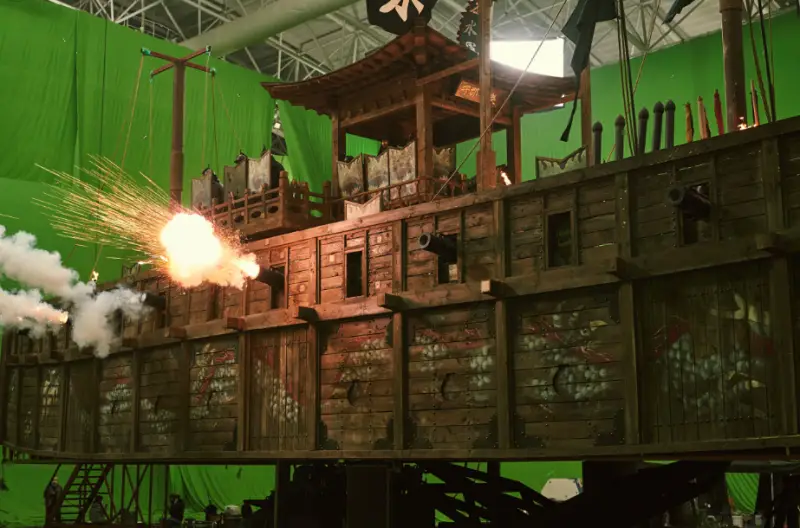 영화노량- 초록색 배경 앞 판옥선 세트에서 불을 뿜어내는 이미지