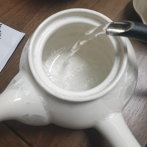 뚜껑이 열린 다완에 뜨거운 물을 붓고 있다.