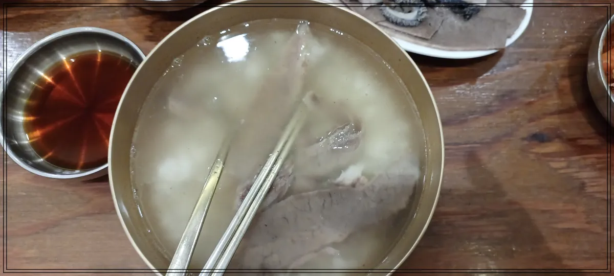 테이블위-왼쪽에-간장이-들어있는-작은-그릇-가운데-국그릇에-곰탕-숟가락과-젓가락이-담겨-있음-밥이-곰탕안에-말아져-있음
