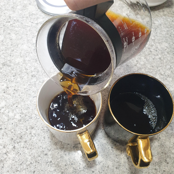 대리석 위에 컵에 커피를 따르는 모습. 검은 컵에는 커피가 담겨 있고 흰 커피에는 커피를 따른다.