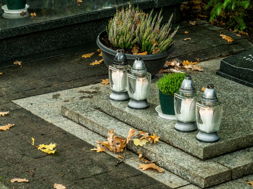 Peaceful cemetery scene with candles and autumn leaves on gravestone.