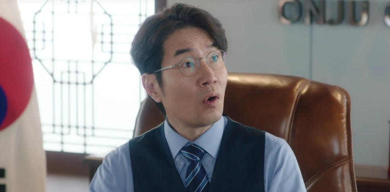 태극기가 있는 시장 사무실을 배경으로 양복을 입고 안경을 쓴 온주 시장이 고급 의자에 앉아 있는 이 연애는 불가항력의 윤학영 캐릭터