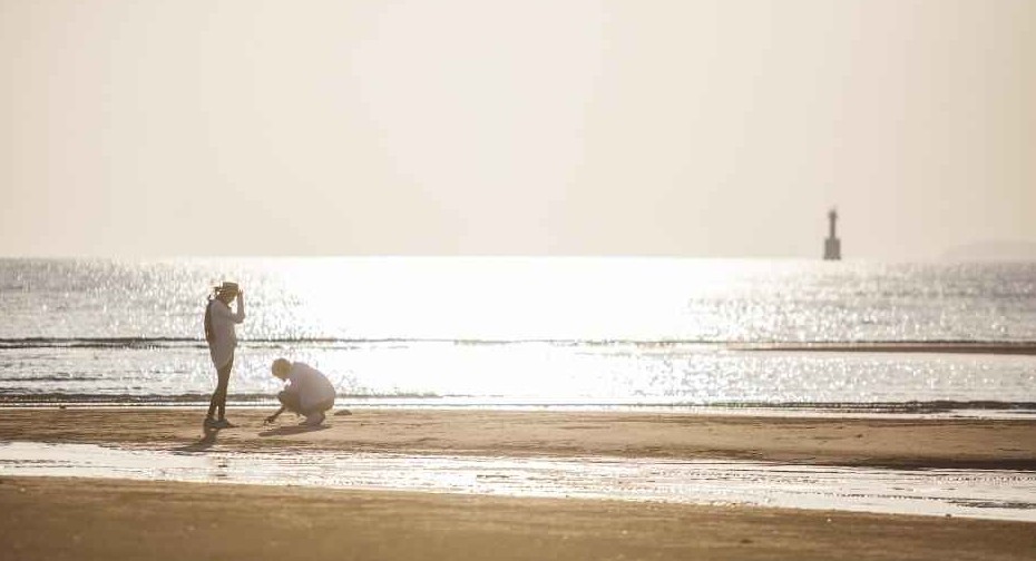 덕적도 해변에서 노을빛 바다를 배경으로 사진을 찍는 사람들. 잔잔한 물결과 부드러운 모래사장, 붉게 물든 수평선이 평화로운 분위기를 자아낸다.
