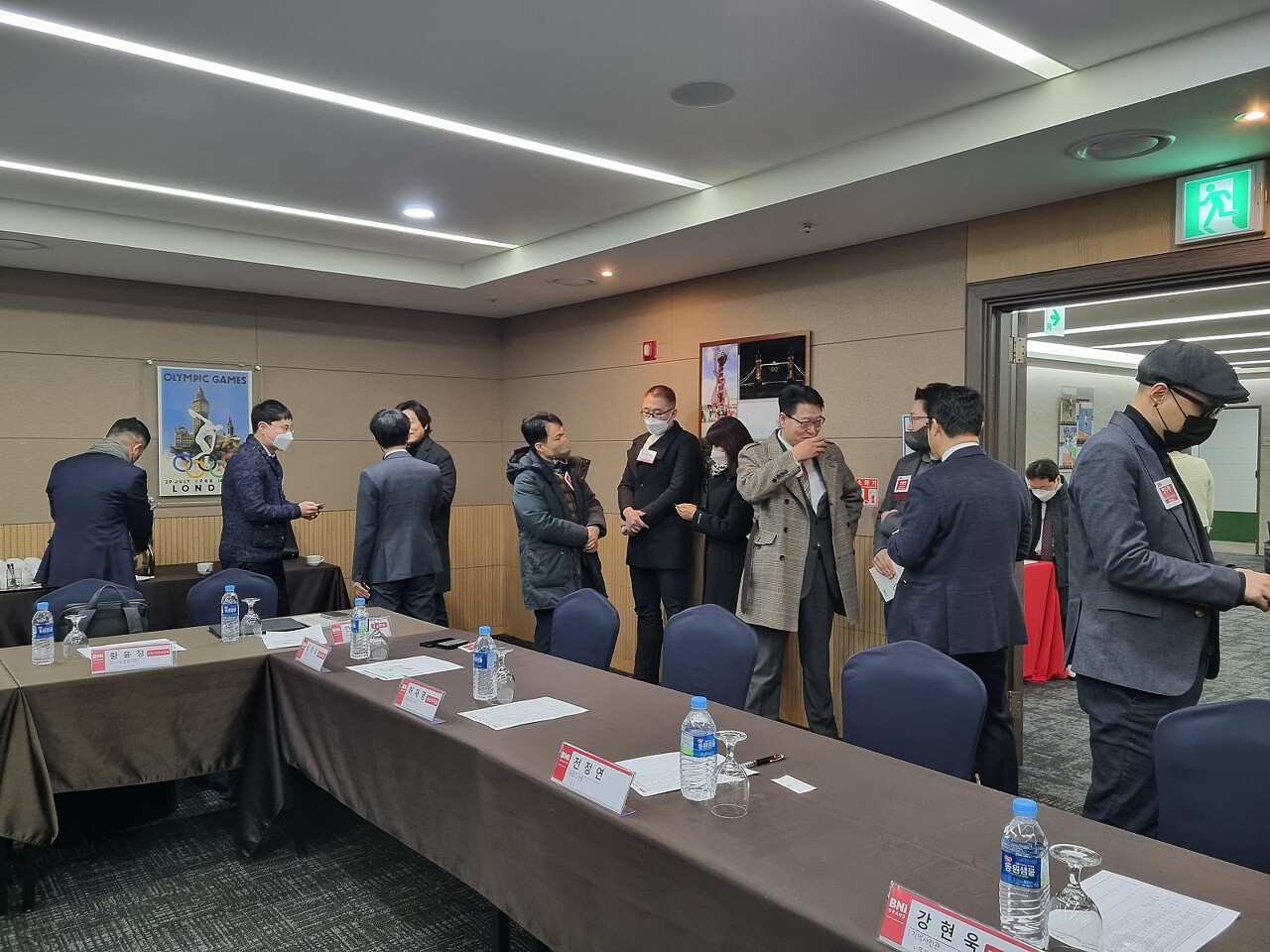 회의실에서 여러 사람들이 비엔아이 모임 시작전 커피를 마시며 이야기하고 있습니다.