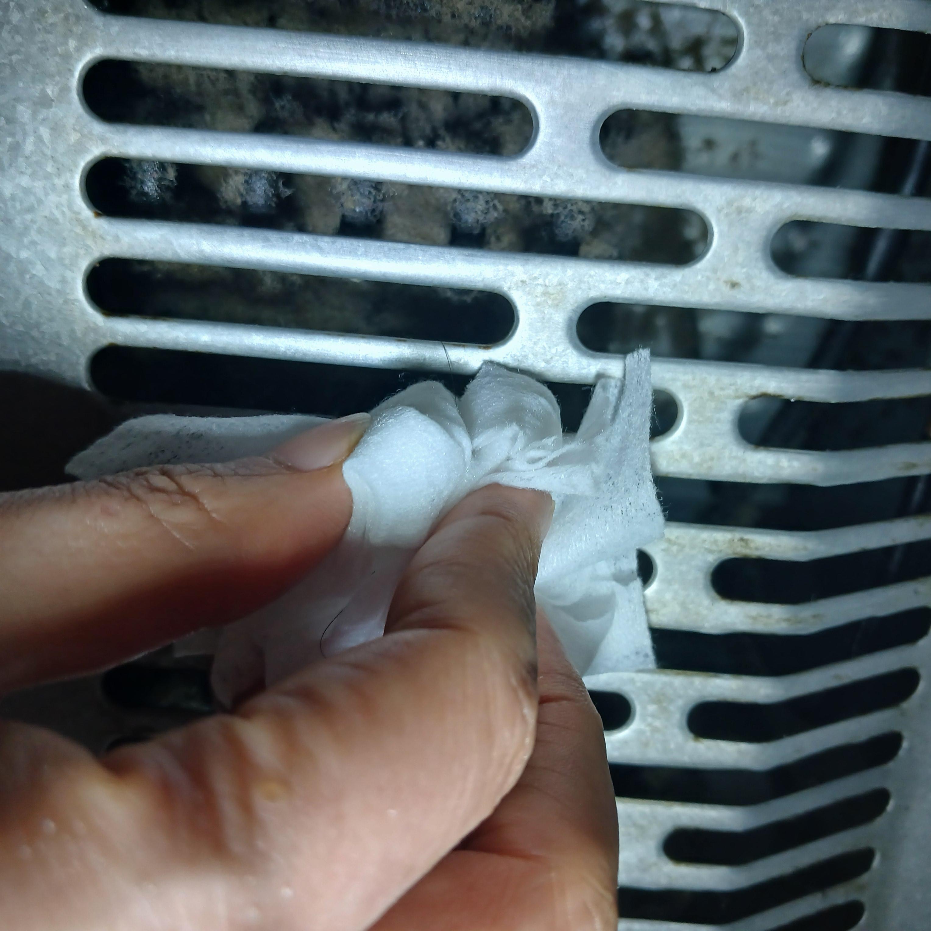 먼지가 쌓인 냉장고 뒷면 그릴을 물티슈로 안전하게 닦아 관리하는 실제 청소 모습