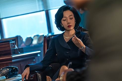 고급스러운 검정 정장을 입은 여성이 사무실에서 손톱을 바라보며 냉정한 표정을 짓는 모습