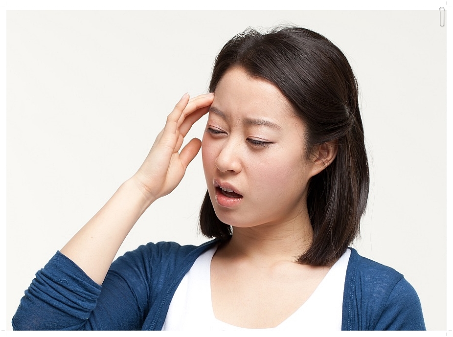 한 손을 이마에 가져다 댄 채 다소 힘겨운 표정을 짓고 있는 여성의 모습