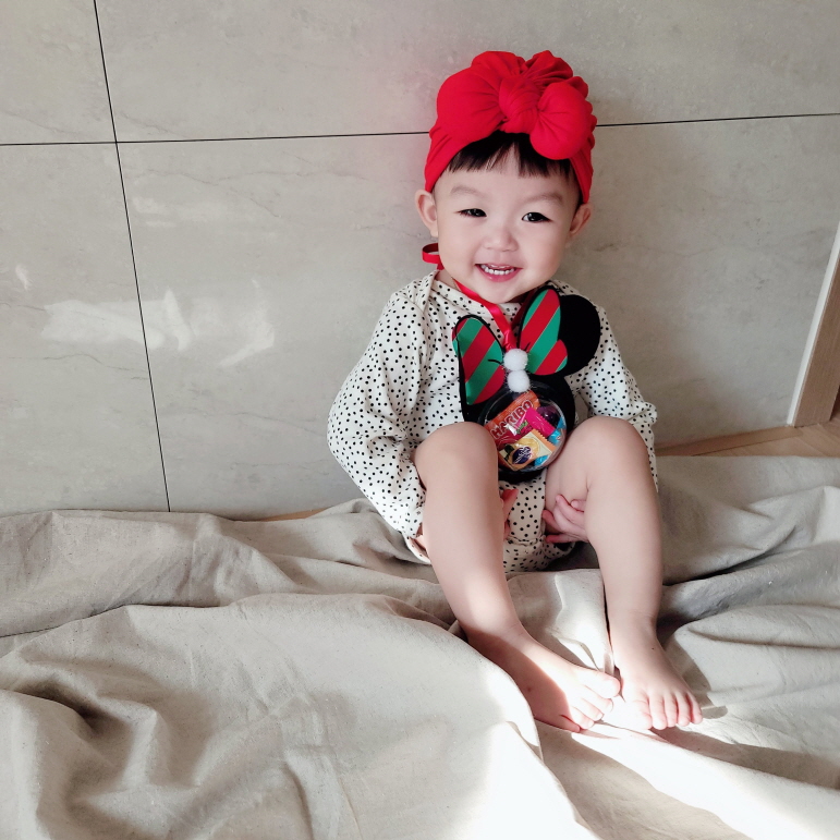 미니마우스 사탕 목걸이를 걸고 앉아서 환하게 웃는 아기모델