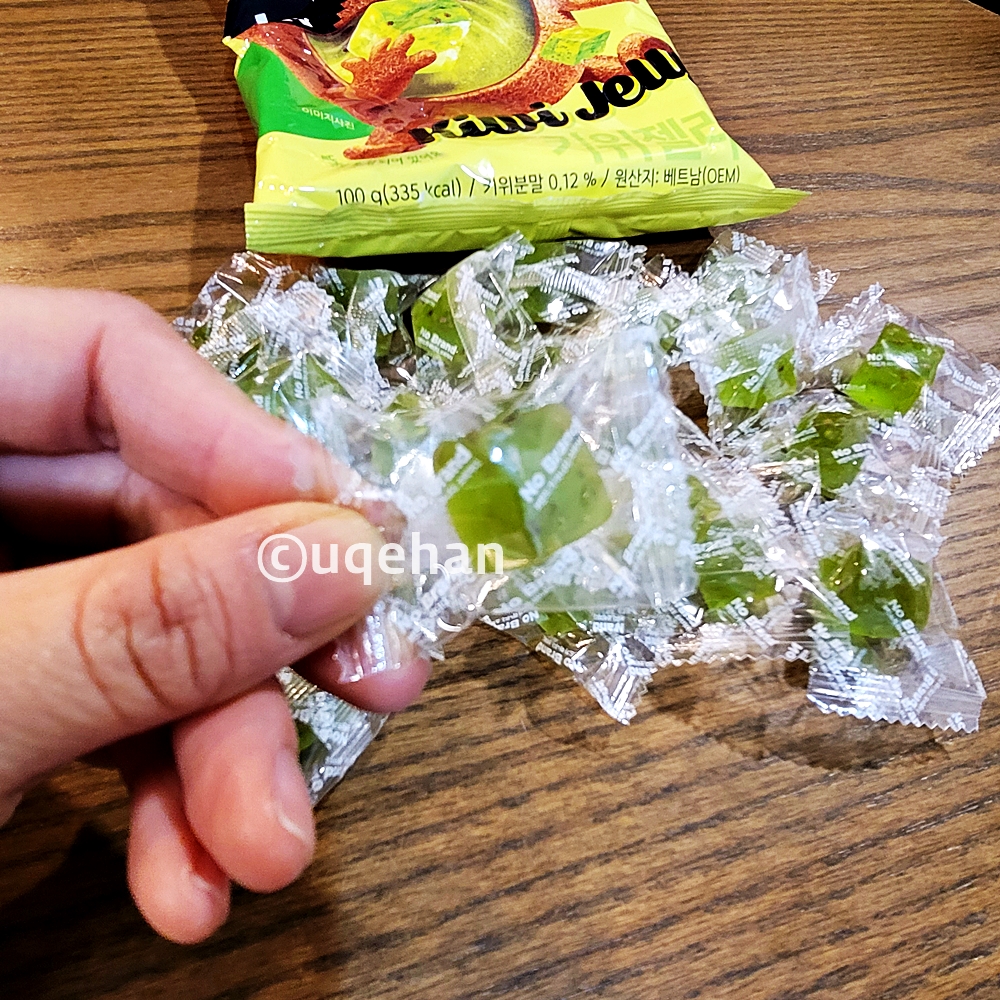 노브랜드 키위 젤리가 테이블 위에 올려져 있고, 개별포장된 젤리를 하나 들고 있다.