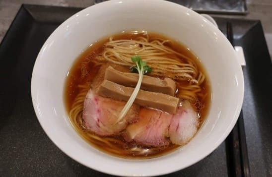 흰색 그릇안에 짙은 갈색의 국물과면 그리고 선홍빛의 고기가 올라가 있다.