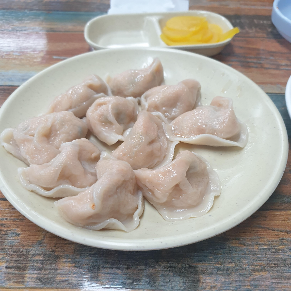 흰 접시 위에 붉은색 만두소가 보이는 김치만두 10개가 올려져있다.