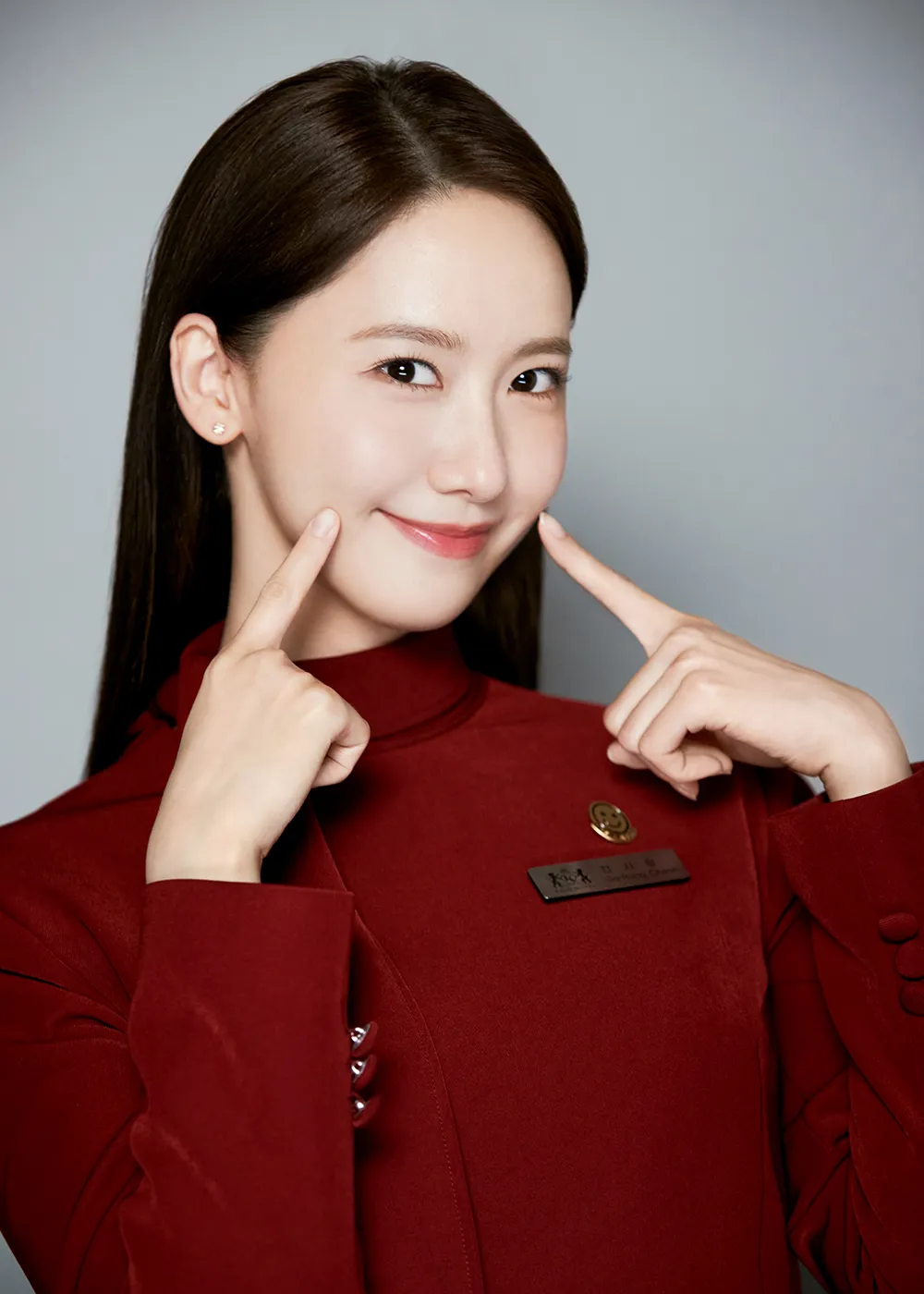 흰색 배경에 킹더랜드 빨강색 사원복을 입고 두 손가락은 입술 양 끝을 가리키며 환하게 웃고 있는 긴머리의 천사랑