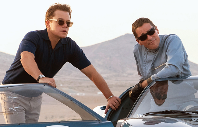 영화 포드 V 페라리에서 두 주인공이 자동차 문에 기대어 사막 트랙을 바라보는 장면