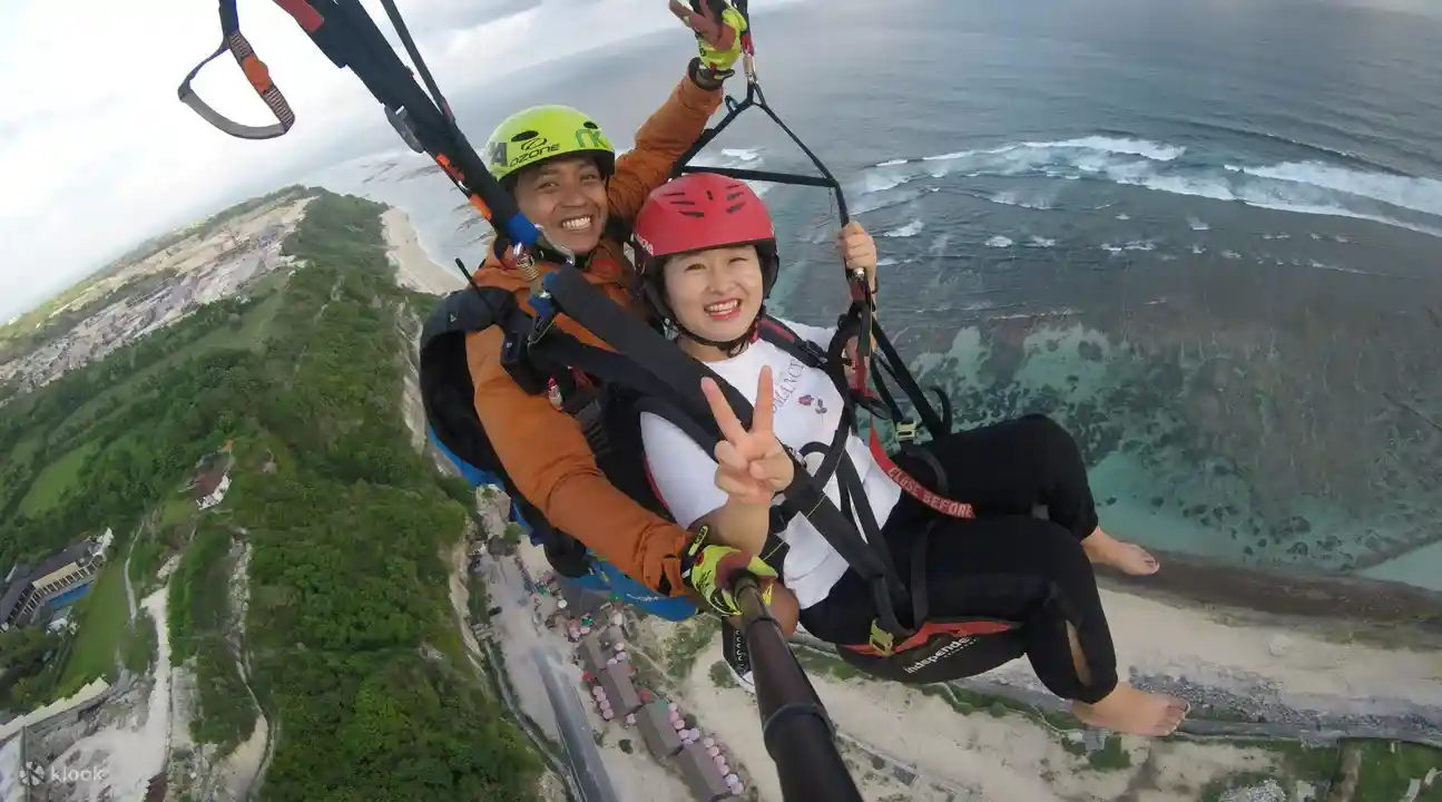 발리 패러글라이딩 예약으로 팀비스 해변 상공에서 전문 파일럿과 함께 탠덤 비행을 하며 바다 절벽을 감상하는 모습