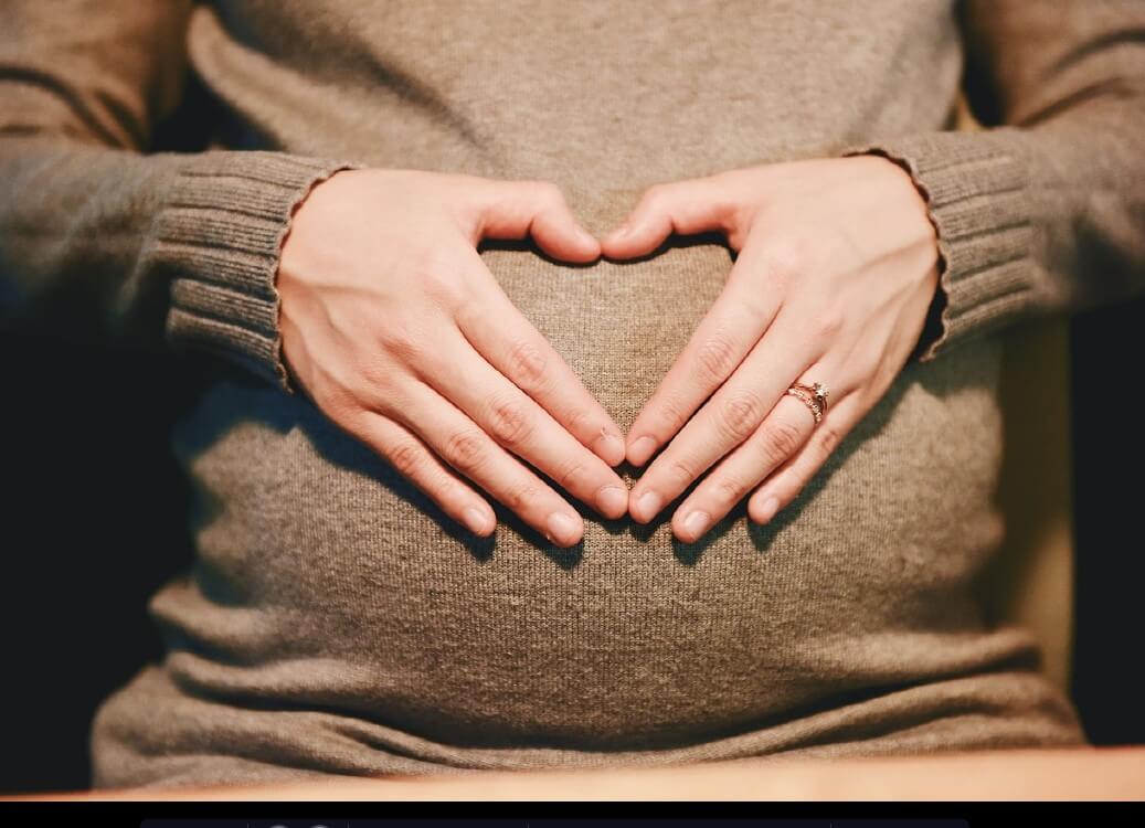 여성이-임신한-자신의-배-위에-손으로-하트를-만들어-보이고-있습니다.