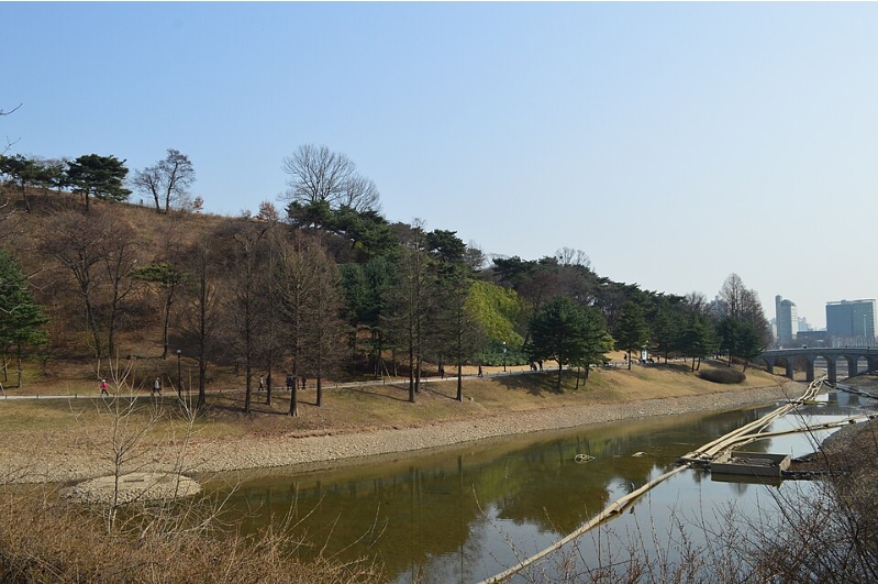 서울 몽촌토성의 흙으로 된 성곽과 주변 물길, 나무가 보이는 풍경