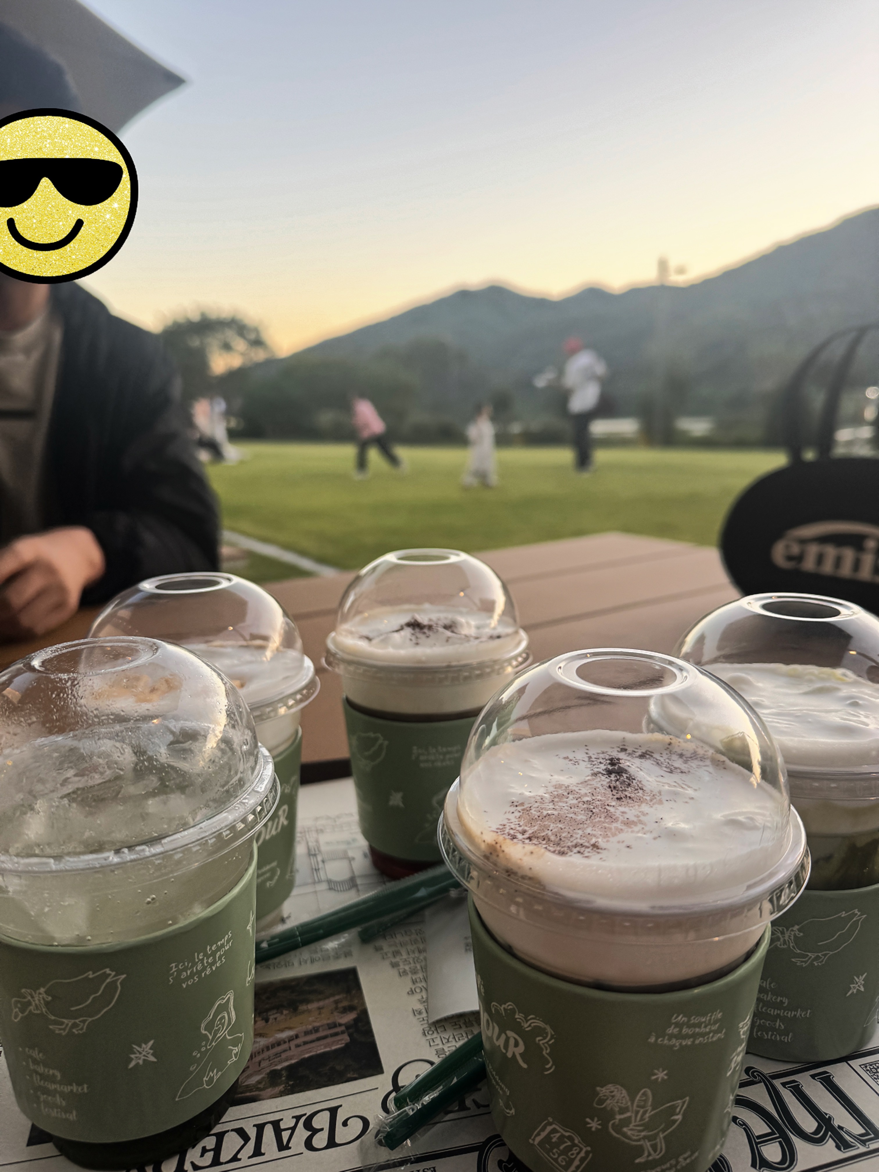 봉주르 팔당 야외 테이블 위 음료들,. 뒤 배경 잔디밭에서는 뛰어노는 아이들과 아빠들이 보인다.