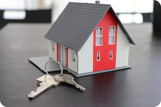 빨간색과 흰색이 조화를 이루는 작은 주택 모형과 열쇠가 함께 놓여 있는 이미지.