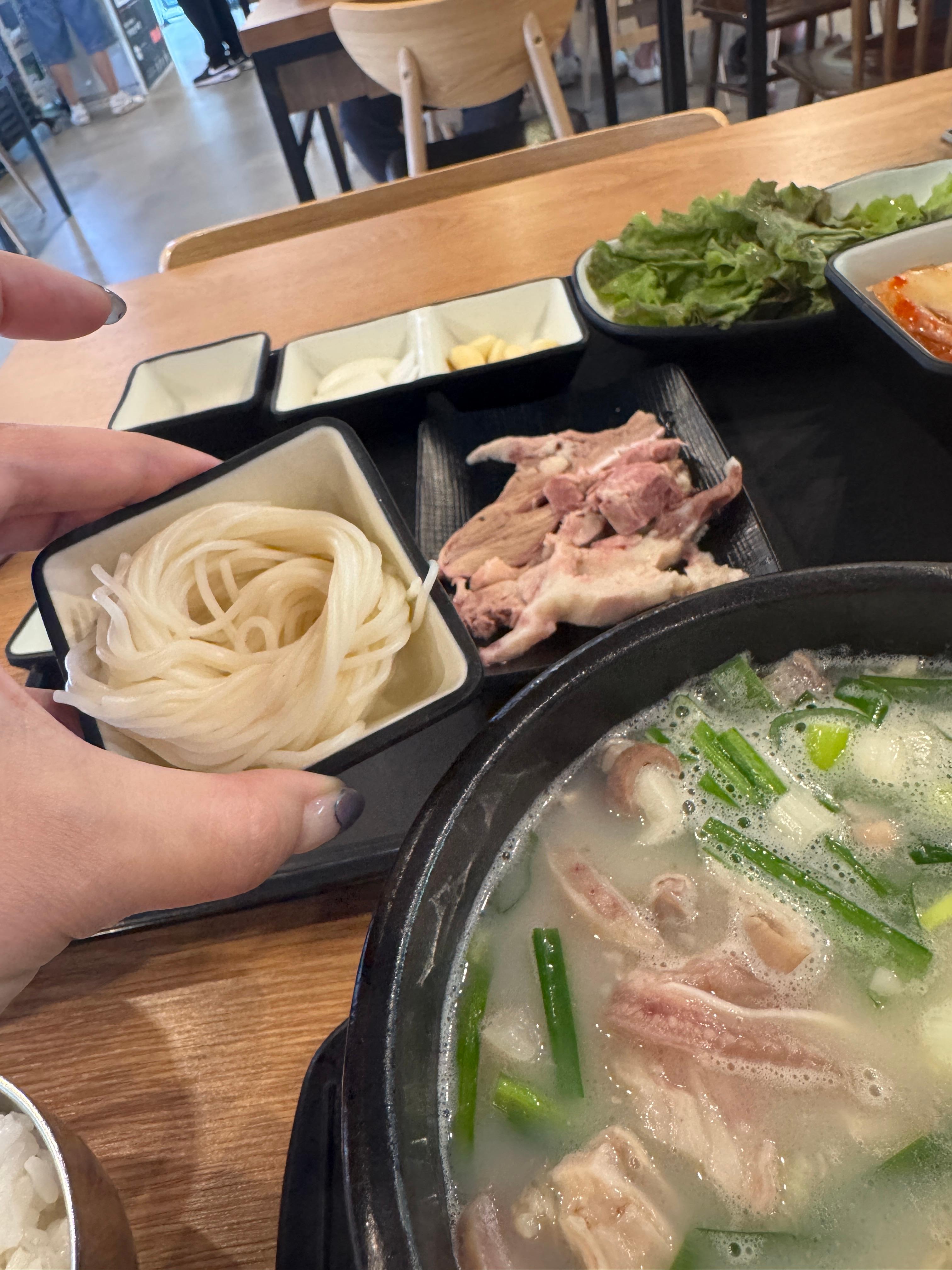 경자국밥 섞어국밥과 함께 제공된 소면을 손으로 들어 올린 모습. 테이블에는 수육&amp;#44; 쌈채소&amp;#44; 밑반찬이 차려져 있다.