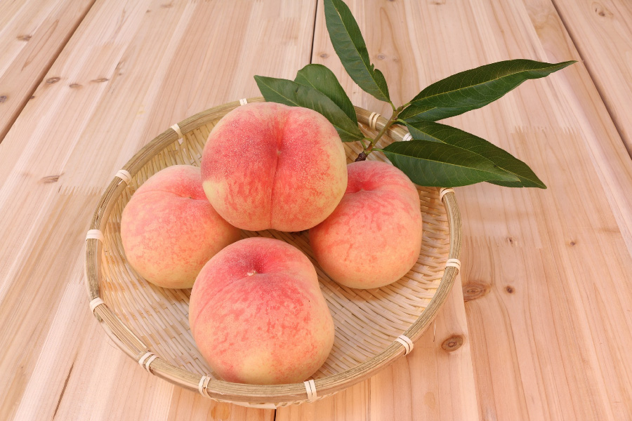야생에서 채취를 한 복숭아를 깨끗하게 세척한 후에 마룻바닥 위에 동그란 대나무 소쿠리를 놓아두고 그 위에 복숭아 4개와 잎을 놓아두고 찍은 사진